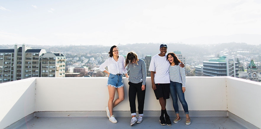 Four University of Otago students relaxing on a balcony above the main campus