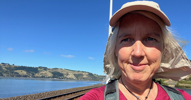 Jennifer Andrewes with the Otago Peninsula behind her. The Otago languages and history alumna has undertaken three pilgrimages after a diagnosis of early-onset Parkinson’s. 