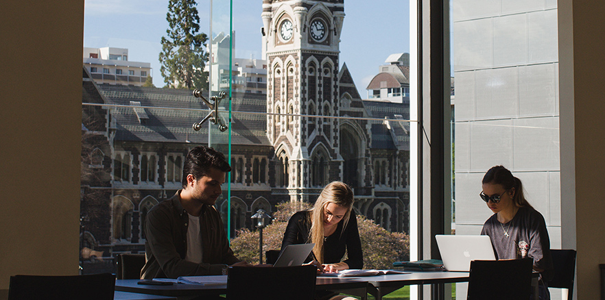 Students studying across the river from the Clocktower Building at University of Otago
